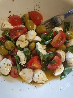 a white bowl filled with tomatoes, mozzarella and green olives next to a fork