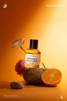 a bottle of perfume sitting on top of a rock next to an orange and flower