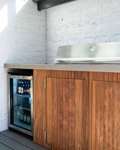 an outdoor kitchen with wooden cabinetry and stainless steel counter top, built into the side of a white brick wall