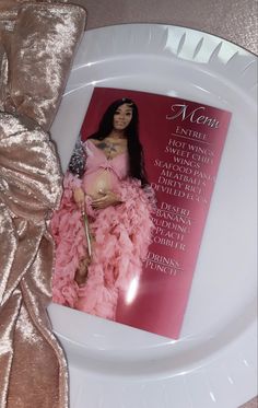 a white plate topped with a magazine and a pink dress on it's cover