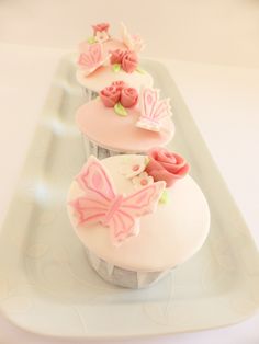 three cupcakes decorated with pink icing on a white platter in the shape of butterflies