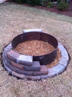 an outdoor fire pit made out of bricks and gravel in a yard with grass around it