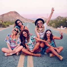 group of women sitting on the side of an empty road posing for a photo with their arms in the air