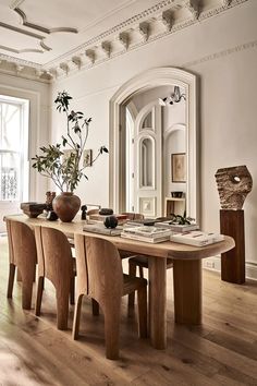 a dining room table with chairs and a vase on it in front of a mirror