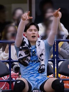 a young man sitting in the bleachers with his arms up and hands raised