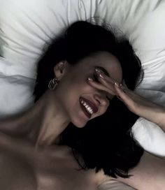 a woman laying in bed with her hands on her face and eyes closed, smiling