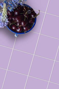 a blue bowl filled with cherries on top of a purple tiled floor