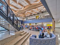 people are sitting in chairs and talking inside an open building with stairs leading up to the second floor