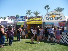 people are lined up to buy lemonade at an outdoor vendor's booth on the grass