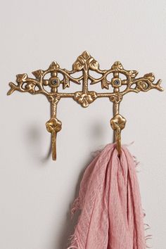 a gold coat rack with two keys and a pink scarf hanging from it's side