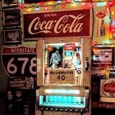 a vending machine is lit up with christmas lights and coca - cola signs on the wall