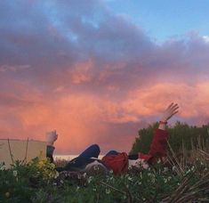 two people laying on the ground with their arms up in the air as the sun sets