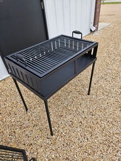 a grill sitting on top of a gravel ground next to a white building with a black door