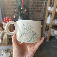 a hand holding a coffee mug with a drawing on the inside and writing on the outside