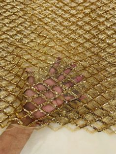 a person's hand is shown through the mesh on a piece of gold cloth