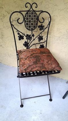 a wrought iron chair with a cushion on it's back and seat pad in front of a stucco wall