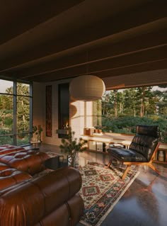 a living room with leather furniture and large windows looking out onto the trees outside at sunset