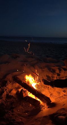 a campfire is lit on the beach at night