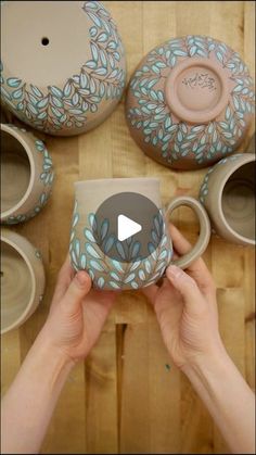 a person holding a coffee mug in front of several pottery bowls and cups on a table