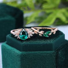 an emerald colored ring with leaves on the band and diamonds in the middle, sitting on top of a green velvet box