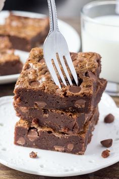 a fork is stuck into some brownies on a plate with milk and chocolate chips