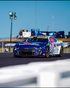 a blue car driving down a race track next to a white fence and light pole