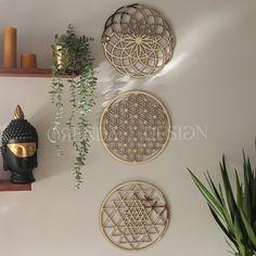 three decorative wall hangings on the wall above a buddha statue and a potted plant