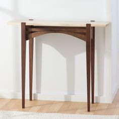 a small wooden table sitting on top of a hard wood floor next to a white wall