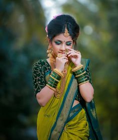 a woman in a green and gold sari holding her hands to her face while standing outside