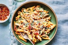 a green bowl filled with pasta and sauce next to a small bowl of seasoning