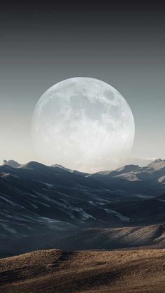 the full moon is seen over mountains in this black and white photo, with no clouds