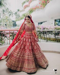 a woman in a red and gold bridal gown standing on a balcony with pink flowers