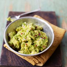 a bowl filled with guacamole sitting on top of a wooden cutting board