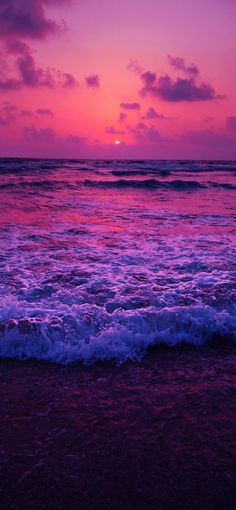 the sun is setting over the ocean with waves crashing in front of it and pink clouds