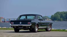 an old black mustang sitting on the side of a road next to a body of water