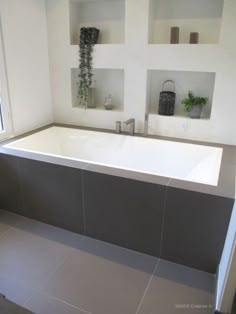 a bath tub sitting next to a window with potted plants on the ledges