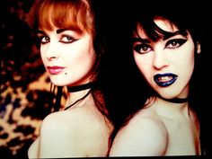 two beautiful young women with dark makeup posing for the camera, both wearing chokers and collars