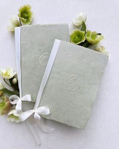 two personalized wedding guest books with ribbons and flowers on the side, sitting next to each other