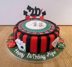 a casino themed birthday cake with dice and playing cards on the top, sitting on a wooden table