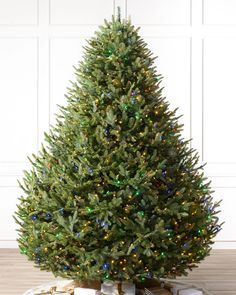 a christmas tree with presents under it on a wooden floor in front of a white wall