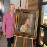 a woman standing next to a painting holding it up