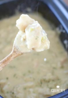 a wooden spoon full of soup with broccoli and dumplings in it,