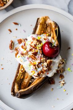 a banana split with ice cream, nuts and a cherry on top sitting on a white plate