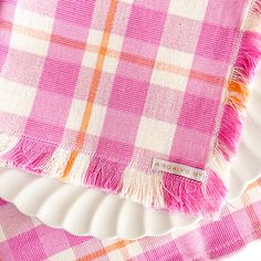 a pink and white checkered table cloth with tassels on it, sitting on a plate