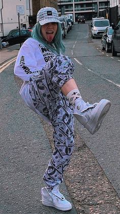 a woman with green hair and white sneakers is skateboarding down the street in front of parked cars