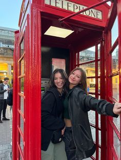 two women standing in a red phone booth