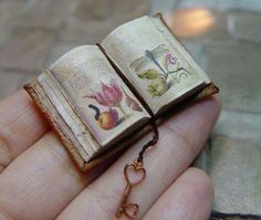 a miniature book is held in the palm of someone's hand with a chain attached to it