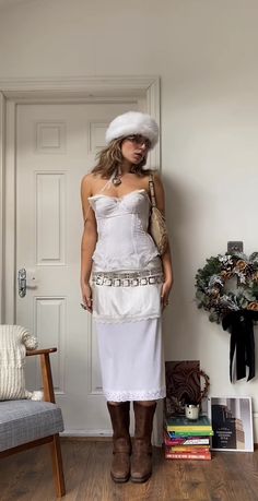 a woman standing in front of a door wearing a white dress and hat with chains on it