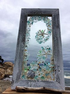 an old wooden frame with sea glass and seashells on it