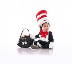 a baby wearing a cat in the hat costume sitting next to a handbag and purse